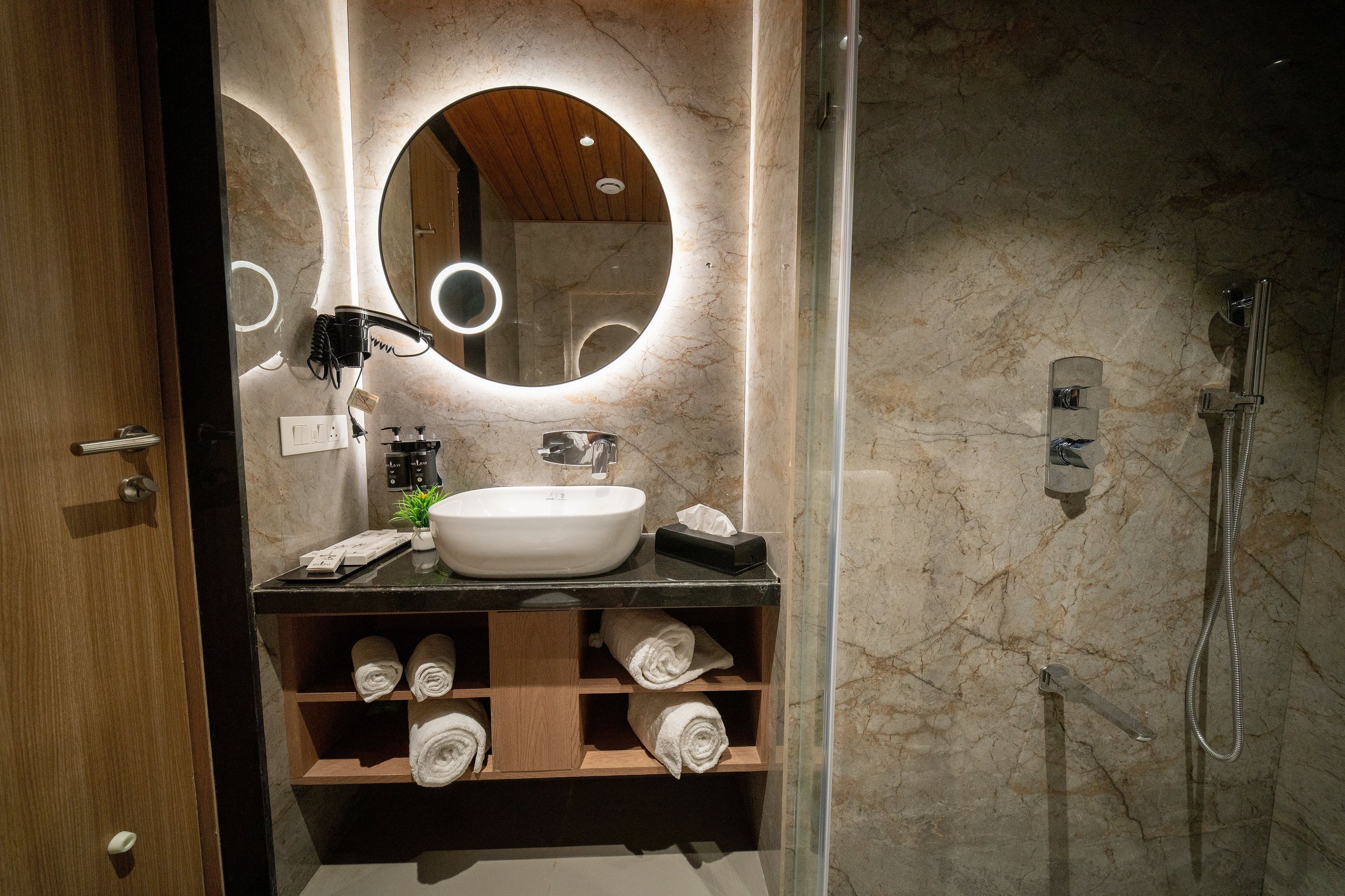 A bathroom with a marble wall, a round mirror, a sink, a towel rack, and a shower.