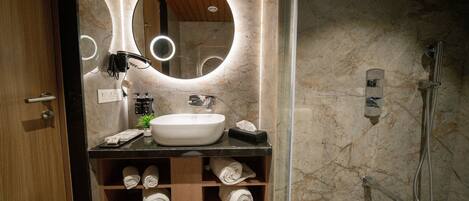 A bathroom with a marble wall, a round mirror, a sink, a towel rack, and a shower.