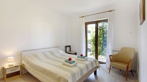 Een slaapkamer met een bed, een stoel, een nachtkastje en een raam met gordijnen.