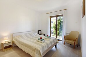 Ein Schlafzimmer mit einem Bett, einem Sessel, einem Nachttisch und einem Fenster mit Vorhängen.