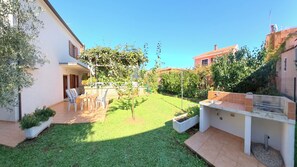 En bostadsträdgård med en uteplats, ett område för grillning och en liten trädgård.