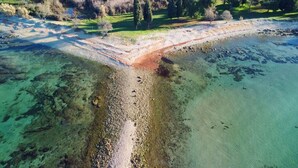 Luchtbeeld van een kustgebied met helder water, een zandstrand en een onverharde weg die leidt naar een begrazen gebied met bomen.