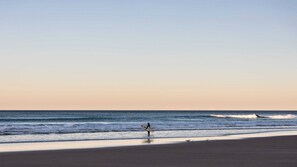 A beach scene with a person holding a surfboard and birds on the sand. - Breakers Block 4 Unit 1 - Lifestyle Yamba (YAMBA)