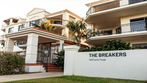 Een hotel met meerdere verdiepingen, een witte gevel, balkons en een bord met de tekst 'THE BREAKERS 18/19 Pacific Parade'.