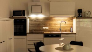 A modern kitchen with white cabinets, a wooden backsplash, a microwave, a coffee maker, and a sink. - Vacation apartment for couples also suitable for dogs (Staudach-Egerndach)