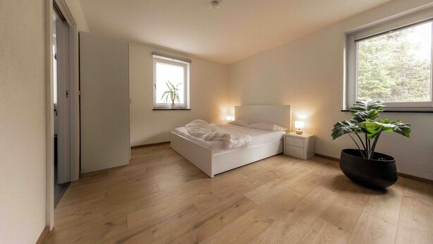 A modern bedroom with a bed, bedside tables, a potted plant, and a window. - Vacation apartment for couples also suitable for dogs (Staudach-Egerndach)