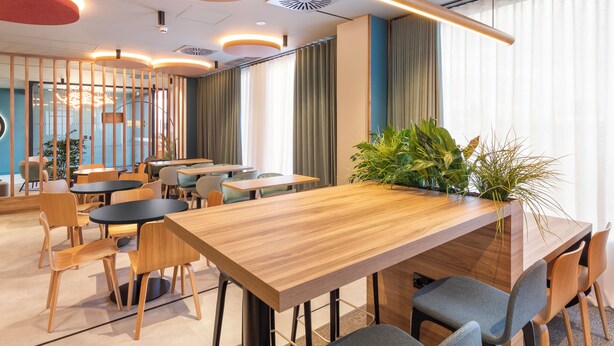 A modern conference room with wooden tables and chairs, a large potted plant, and a view of the city through large windows. - B&B HOTEL Madrid Vallecas La Gavia (Madrid)