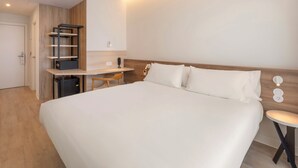 A hotel room with a large bed, a desk, and a chair. There is a small table and a wall-mounted shelf. - B&B HOTEL Madrid Vallecas La Gavia (Madrid)