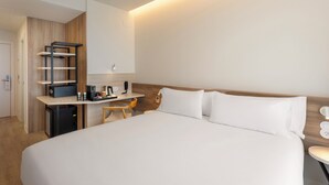 A hotel room with a large bed, a desk with a chair, a small kitchenette, and a wooden wall panel. - B&B HOTEL Madrid Vallecas La Gavia (Madrid)