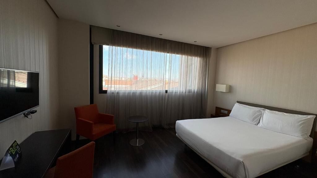 Quarto de hotel com uma cama grande, televisão, escrivaninha e cadeira.