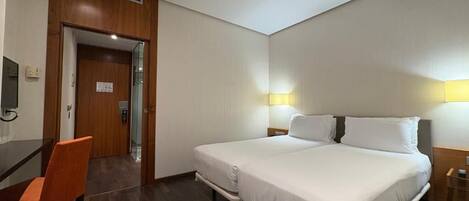 Habitación de hotel con una cama grande, un escritorio y una silla. Se ve una puerta que da al baño y un televisor montado en la pared.