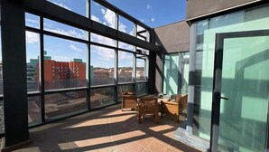 A balcony with large windows, a table, and chairs.