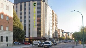 A multi-story hotel with a prominent 'B&B' sign on the facade, located on a city street with vehicles and a clear sky.