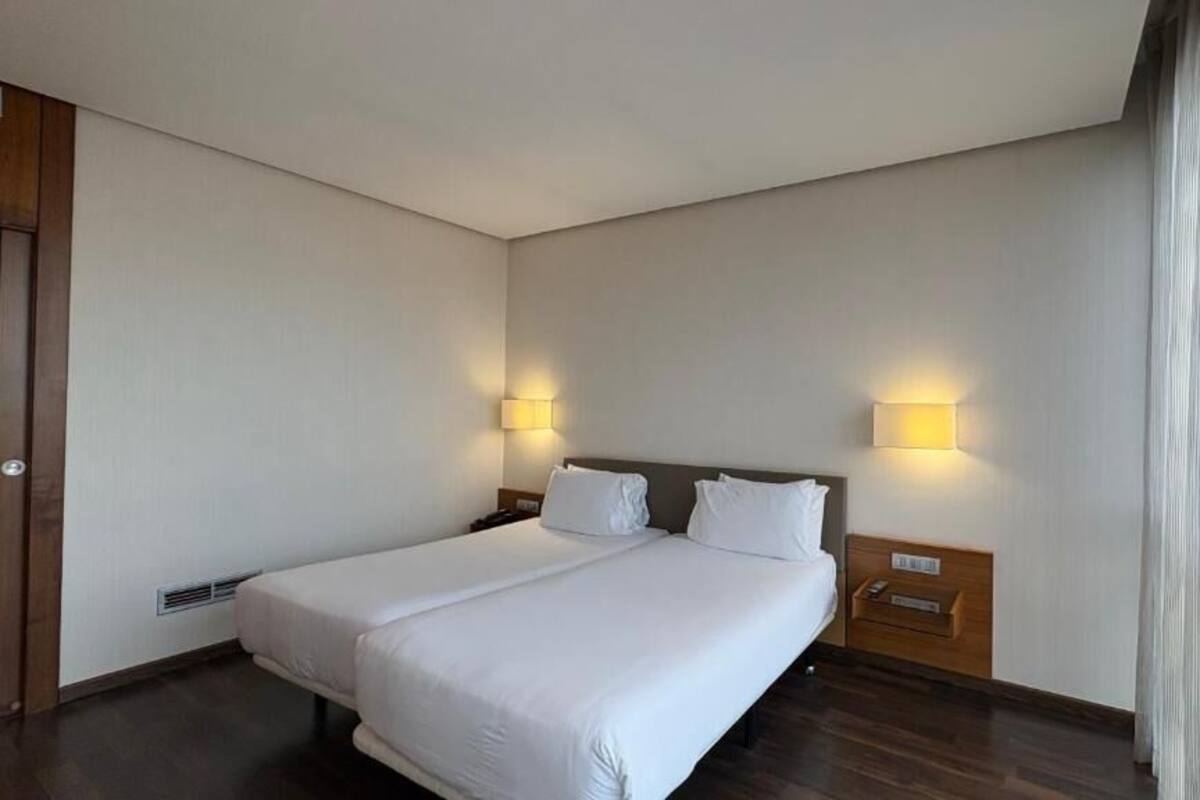Een hotelkamer met een groot bed, twee bedlampen, een houten nachtkastje en een gordijn voor het raam.