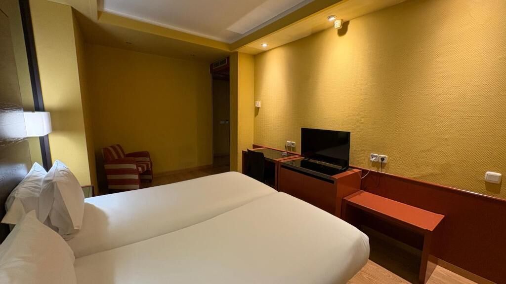 Een hotelkamer met een bed, een bureau met een laptop, een televisie en een stoel.