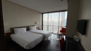 A hotel room with two beds, a TV, a small table, and a balcony with curtains.