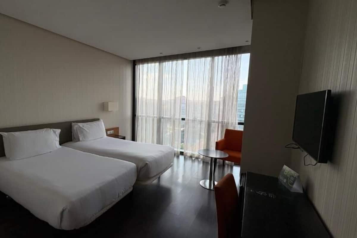 Een hotelkamer met twee bedden, een televisie, een kleine tafel en een balkon met gordijnen.