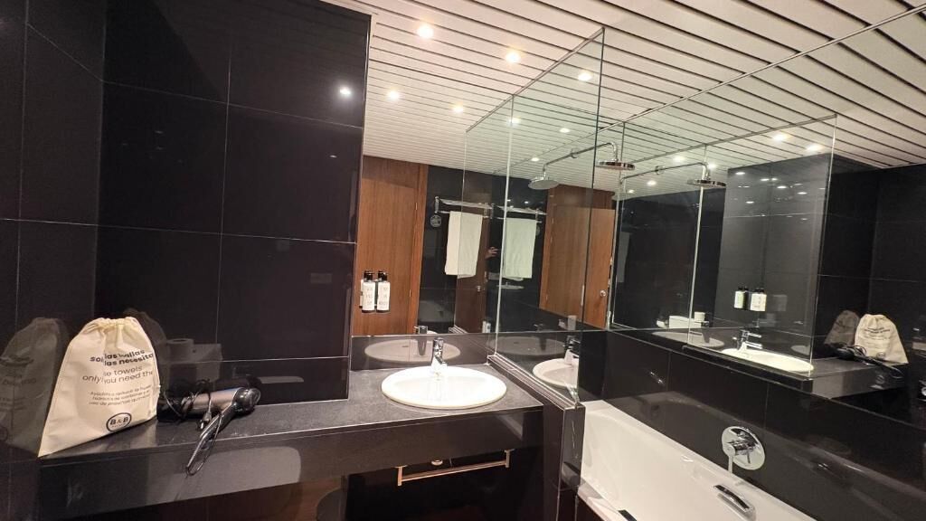 A modern bathroom with dark tiles, a white sink, a glass shower enclosure, and a large mirror.