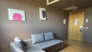 A modern room with a grey sectional sofa, wooden flooring, and two abstract wall art pieces. - B&B HOTEL Miranda de Ebro (Ribera Baja)
