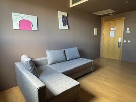 Quarto moderno com sofá seccional cinza, piso de madeira e duas obras de arte abstratas na parede.