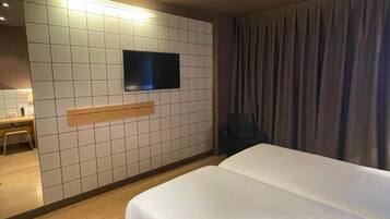 Une chambre d’hôtel avec un grand lit, un téléviseur à écran plat fixé au mur, un bureau avec une chaise et une fenêtre avec des rideaux.