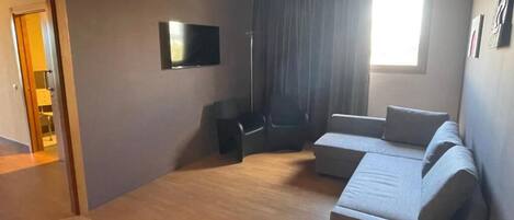 Una sala de estar moderna con un sofá modular, un televisor de pantalla plana montado en la pared y un ventanal con cortinas.