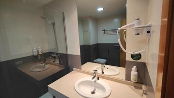 Casa de banho com duas pias, chuveiro e secador de cabelo fixo na parede.