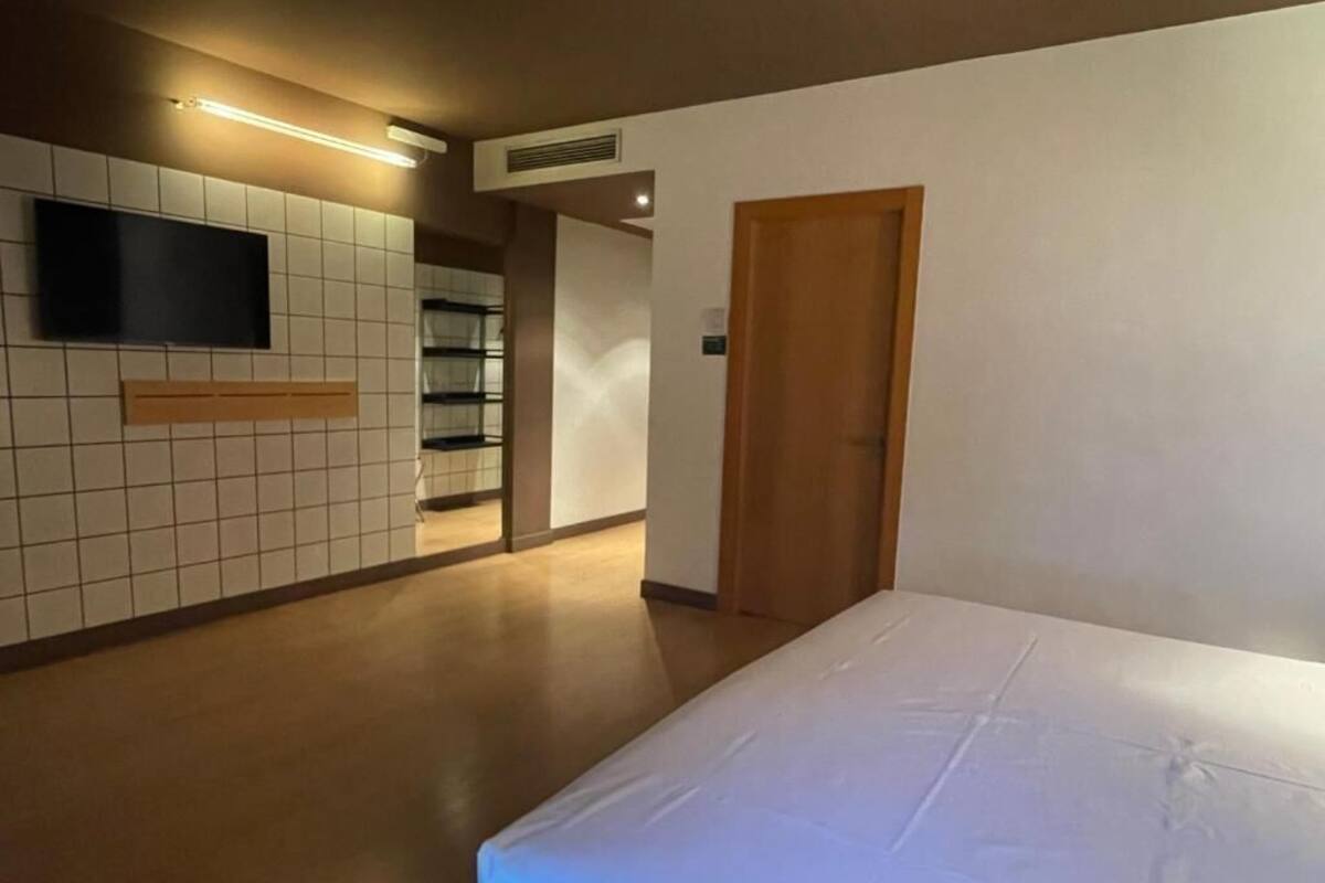A hotel room with a bed, a television mounted on the wall, and a wooden door.