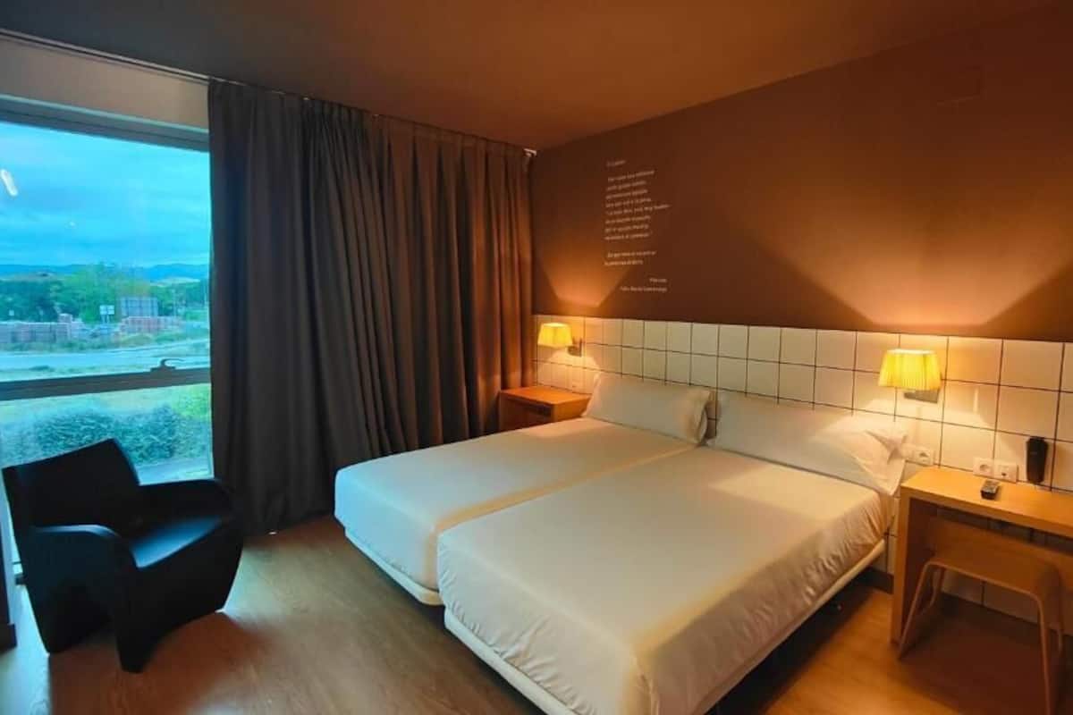 A hotel room with a large bed, two bedside tables with lamps, a chair, and a view of the outside.