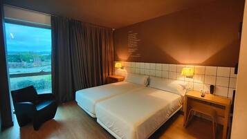 A hotel room with a large bed, two bedside tables with lamps, a chair, and a view of the outside.