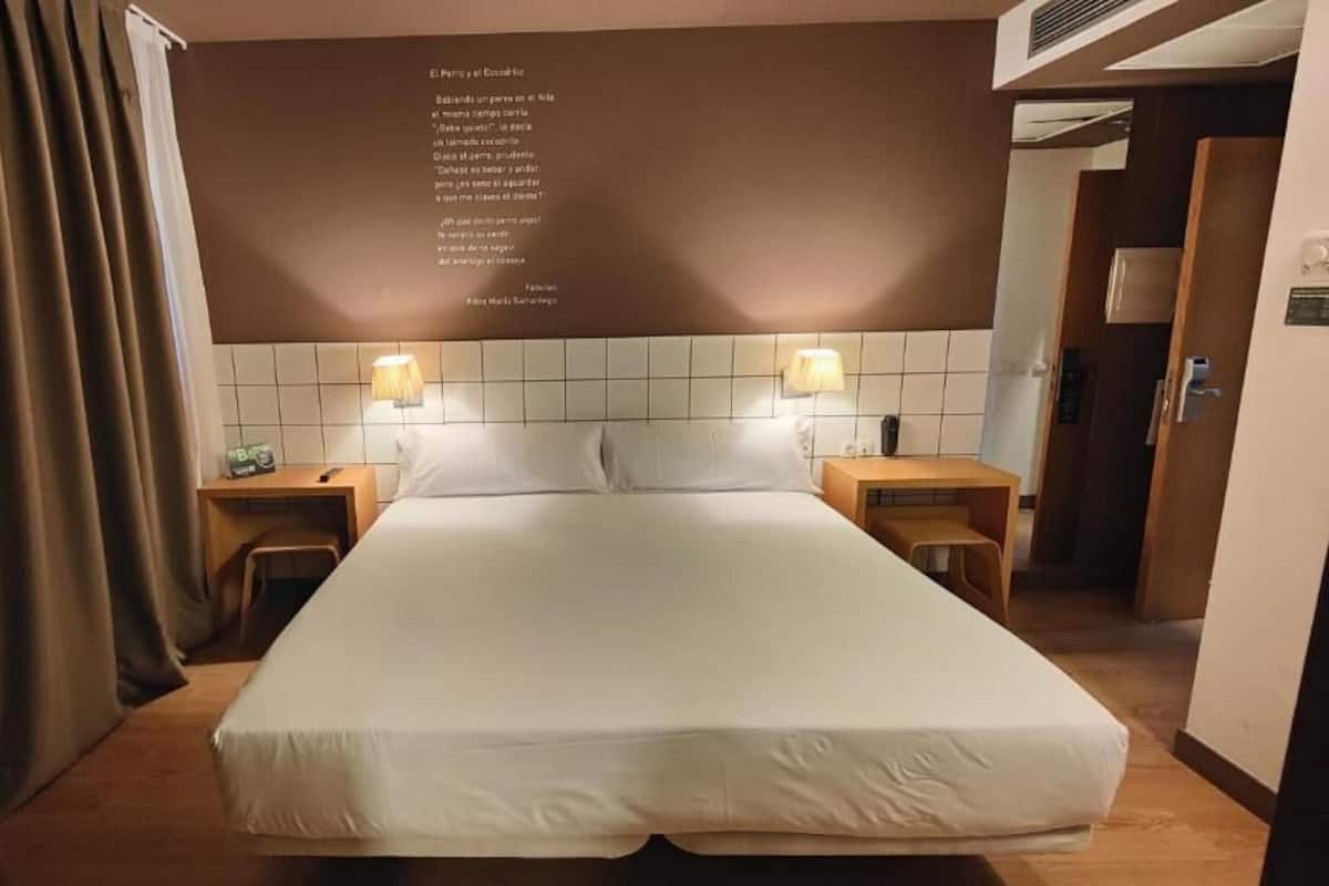 A hotel room with a large bed, two bedside tables, and a wall with a poem.