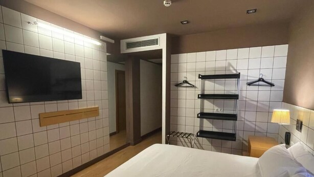 A hotel room with a bed, a TV mounted on the wall, a towel rack, and a heater. - B&B HOTEL Miranda de Ebro (Ribera Baja)