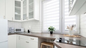 Una cucina moderna con mobili bianchi, un forno a microonde, una macchina del caffè e una finestra con persiane.