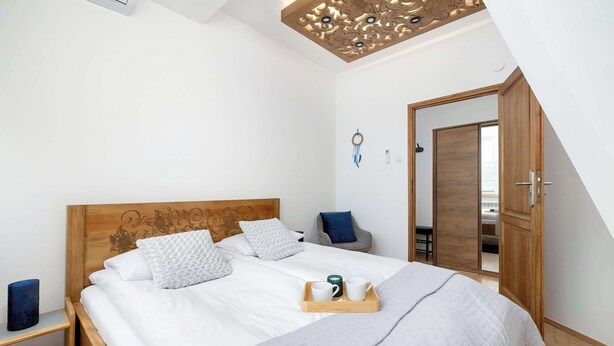 Un letto rifatto con cura, un vassoio con due tazze, una testiera in legno e un soffitto con pannello decorativo.