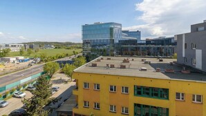 Un edificio moderno con facciata in vetro, un parcheggio e un edificio giallo con molte finestre.