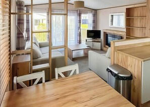 Un espacio habitable compacto con sofá, una mesa de comedor, televisor y zona de cocina.