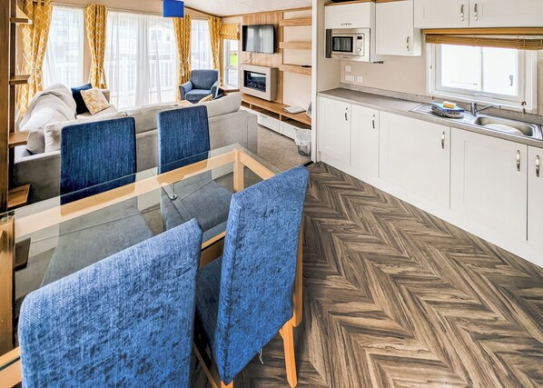 Un interior moderno con comedor, sofá, televisor, cocina y suelo de madera.