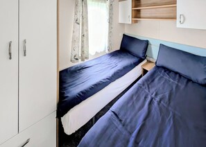 Un dormitorio con dos camas individuales, un armario, una mesita de noche pequeña y una ventana con cortinas florales.