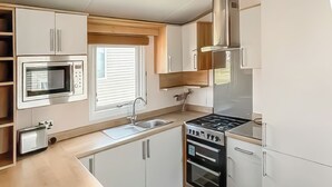 A compact kitchen with a microwave, sink, stove, oven, and wooden cabinets.