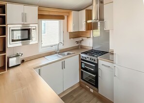 Una cocina compacta con microondas, lavamanos, estufa, horno y armarios de madera.