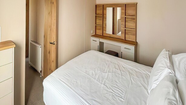 A bedroom with a bed, a wooden wardrobe, a desk, and a radiator.
