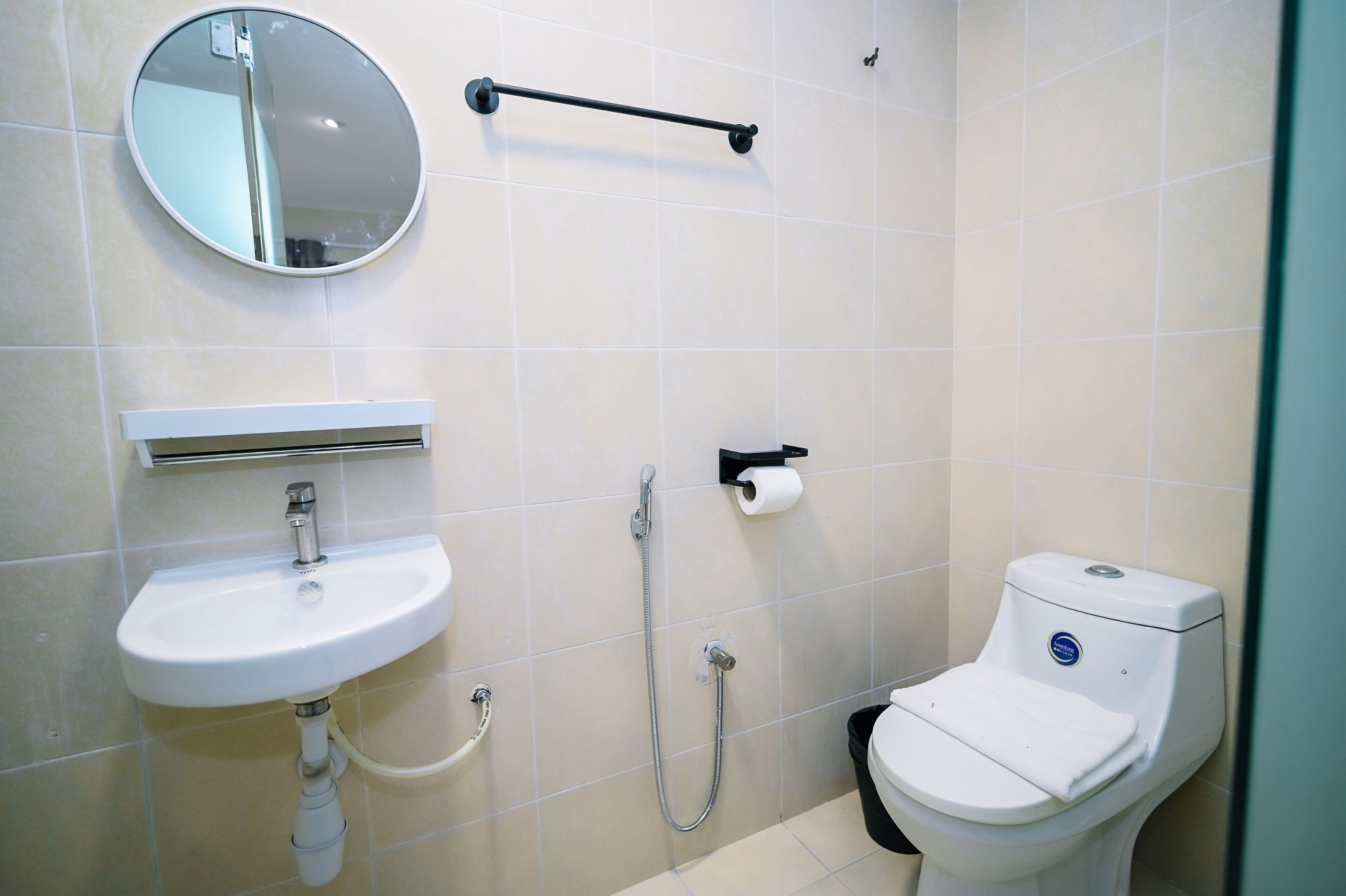 A modern bathroom with a round mirror, a white sink, a toilet, and a shower.