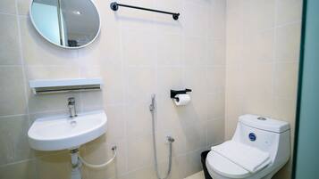 A modern bathroom with a round mirror, a white sink, a toilet, and a shower.