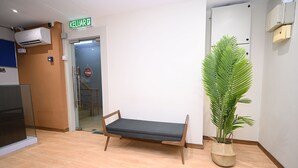 Una habitación con un banco de madera, una planta en maceta y una puerta cerrada con un cartel.