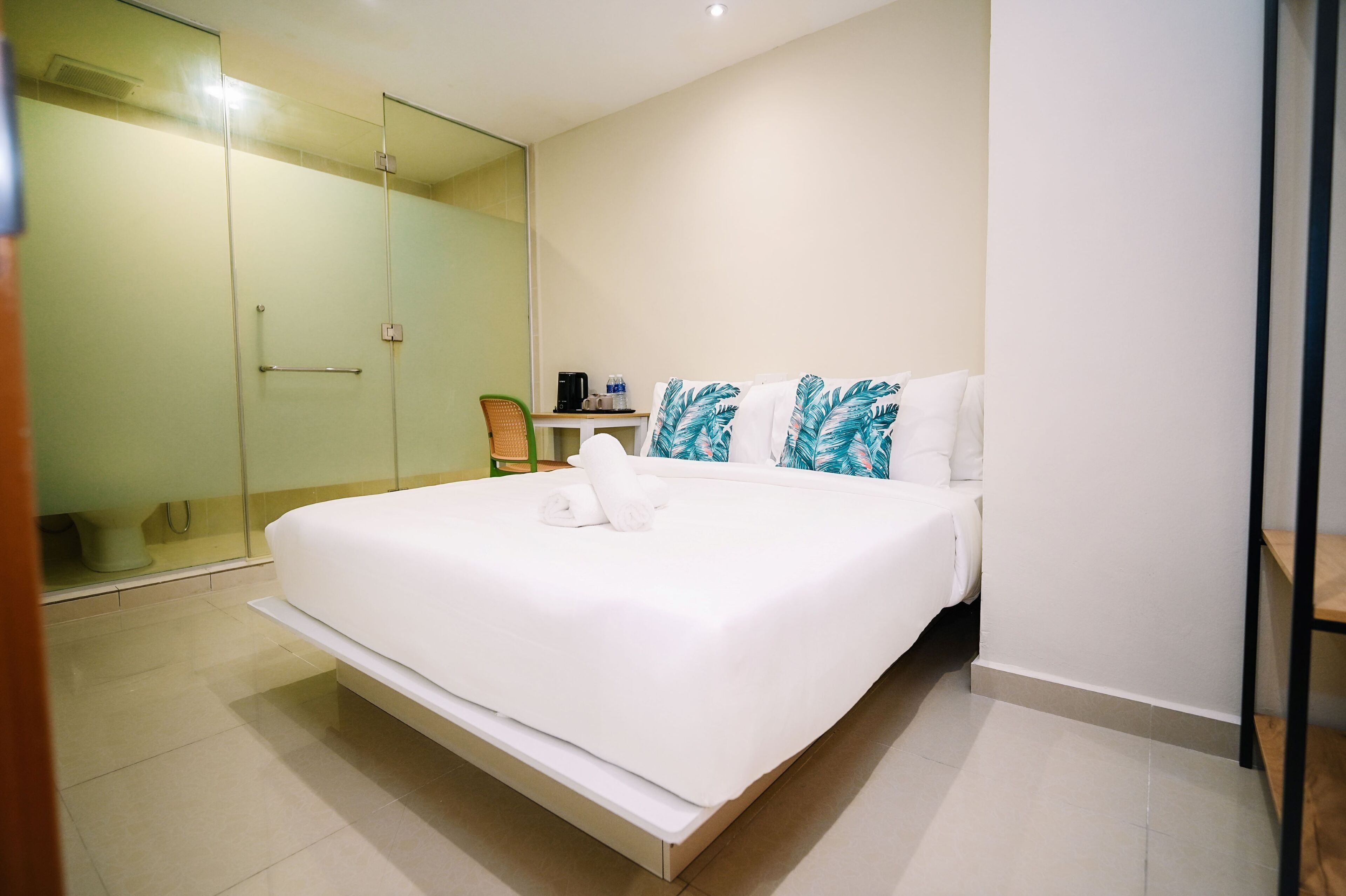 A hotel room with a bed, a chair, a small table with a coffee maker, and a glass shower enclosure.