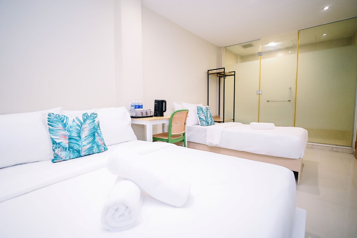 Habitación de hotel con cama, una silla, una mesita con cafetera y zona de ducha.