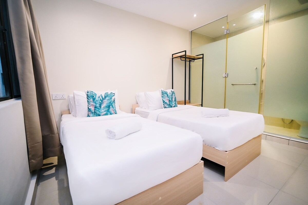 Habitación de hotel con dos camas, cabina de ducha de vidrio y diseño moderno.