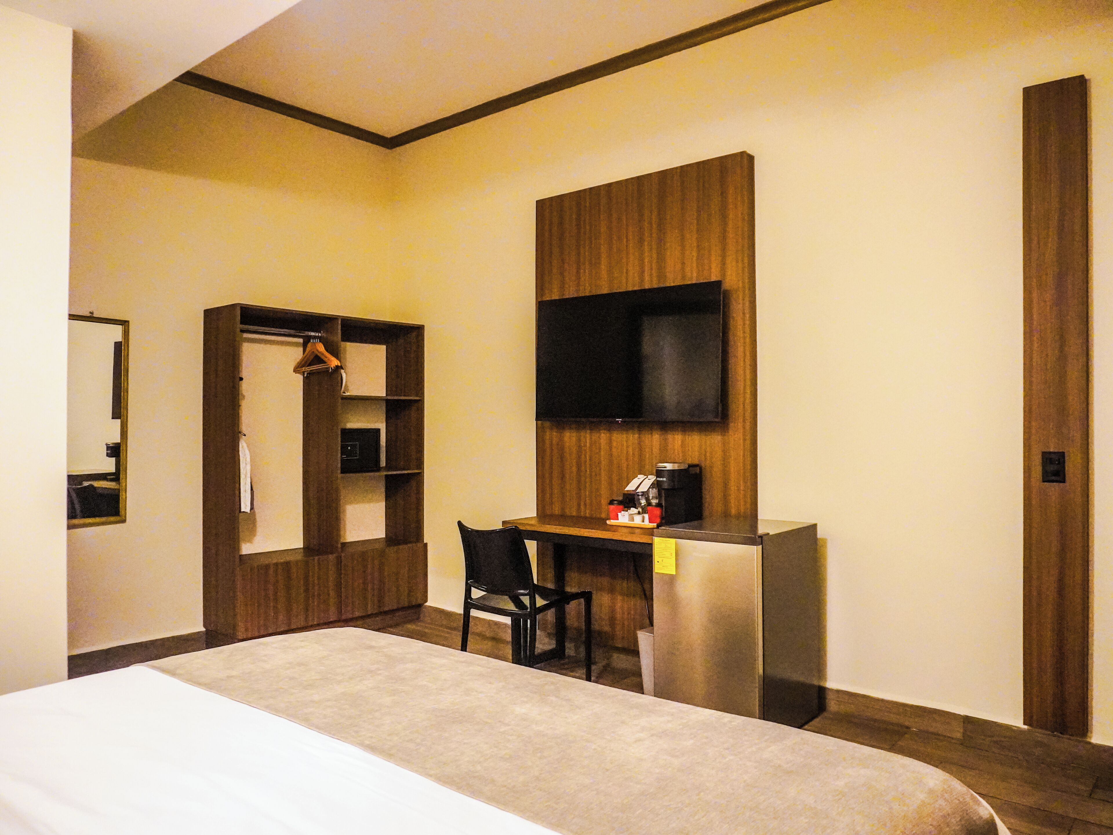 A hotel room with a bed, a desk with a chair, a television, and a wardrobe.