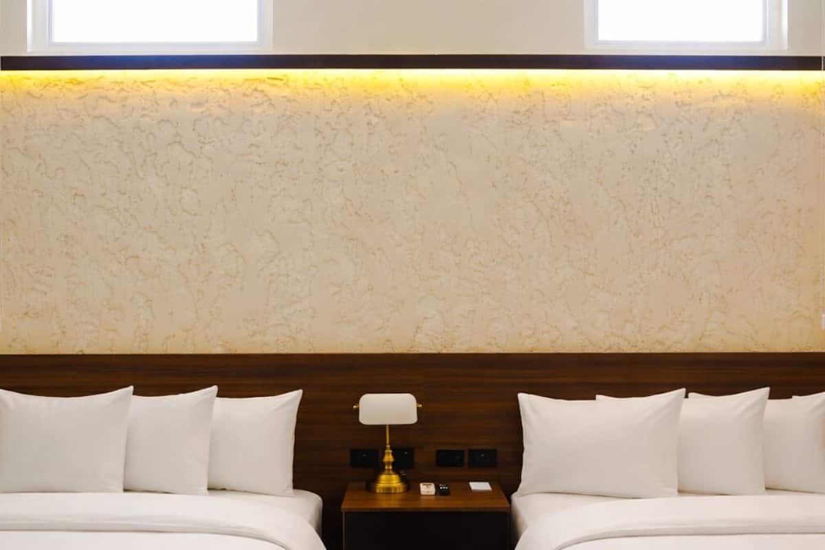 Une chambre d’hôtel avec deux lits, une table de chevet avec une lampe et un mur à texture.