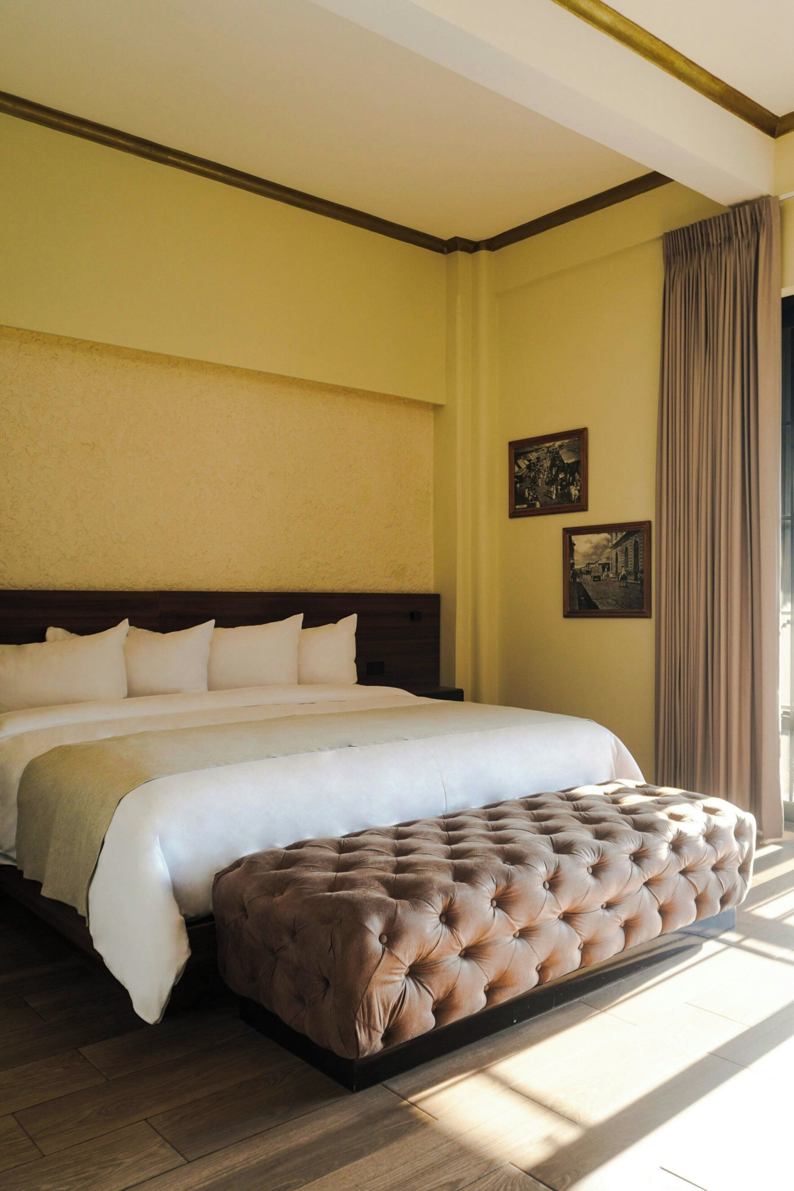 A large bed with a headboard, a tufted ottoman, and two framed pictures on the wall.